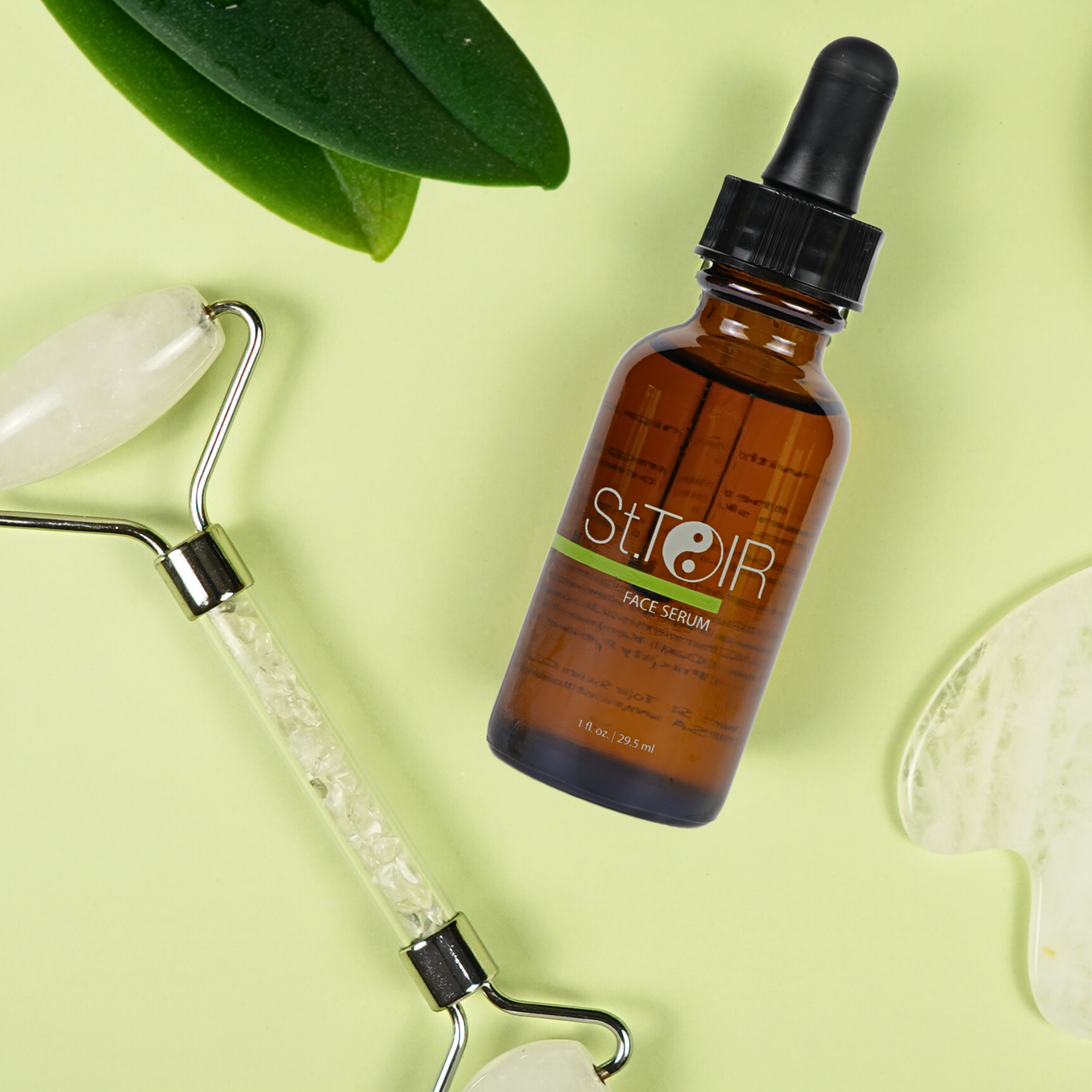 Brown bottle of St.ior face serum with a roller and green leaves on a light green background