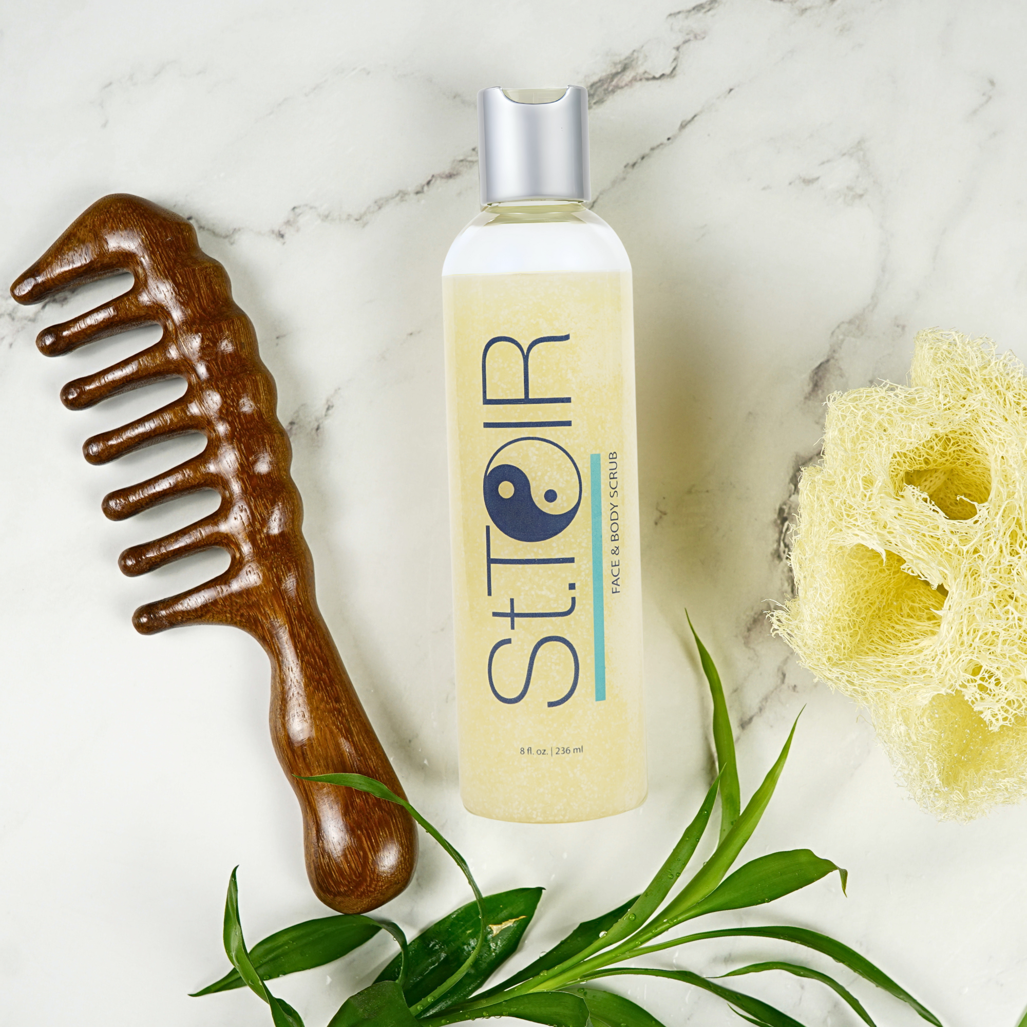 Bottle of St. Theraputic face and body serum with a wooden comb and sponge on a marble surface.